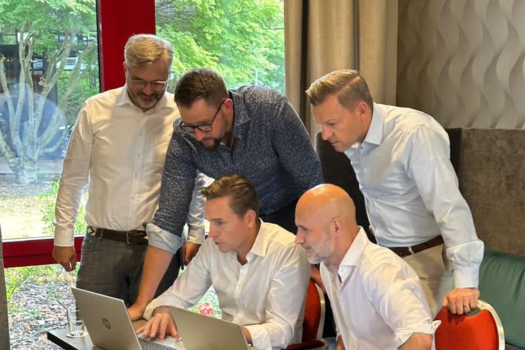 Fünf Teilnehmer stehen und sitzen um zwei Laptops und bauen gemeinsam an einer Anwendung