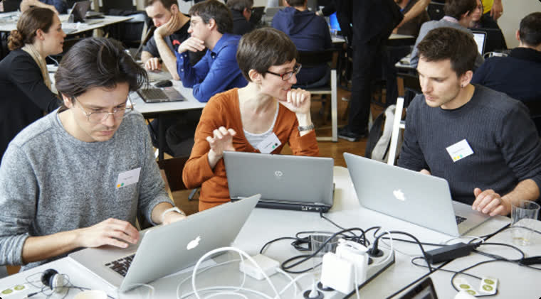 Teilnehmer an Laptops an einem langen Tisch in einem Workshop-Raum